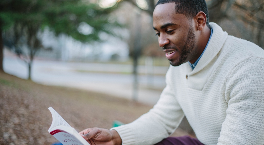 Man in white sweater reading a book