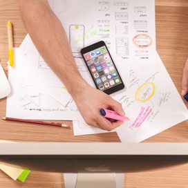 Someone writing on a desk with papers and a smart phone on top